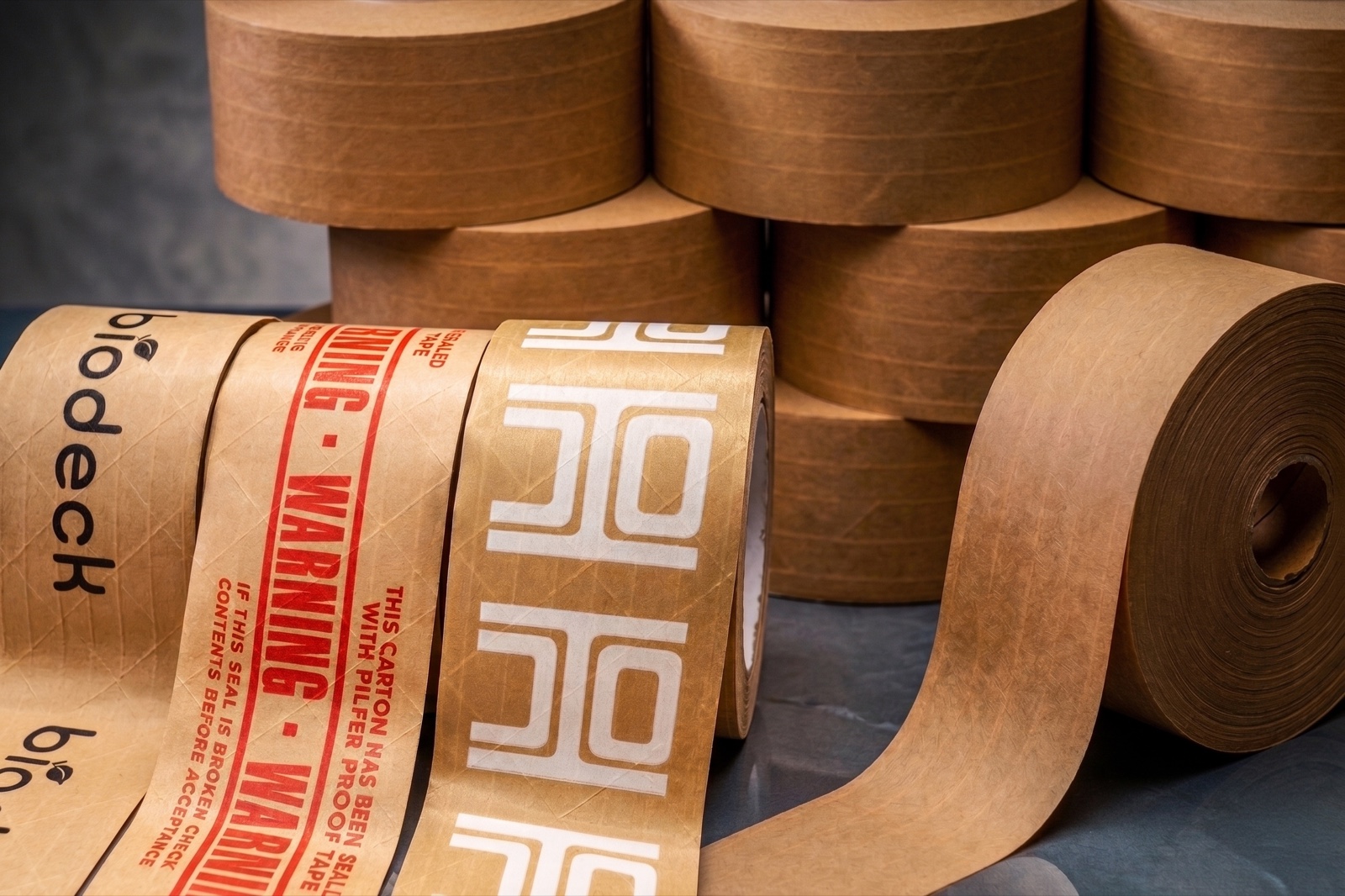 Stacked rolls of kraft water-activated paper tape with one roll unrolled across the top — reinforced gummed tape for case sealing