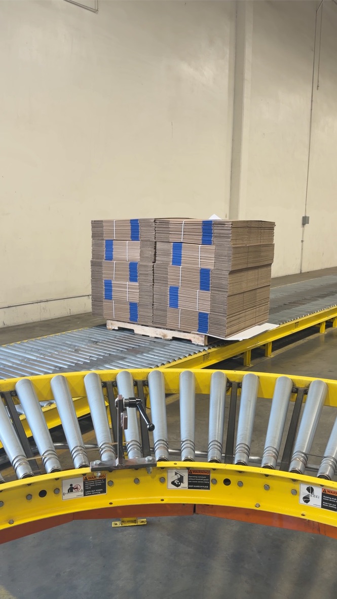 Pallet of die-cut corrugated blanks moving down the production conveyor at Rox Packaging